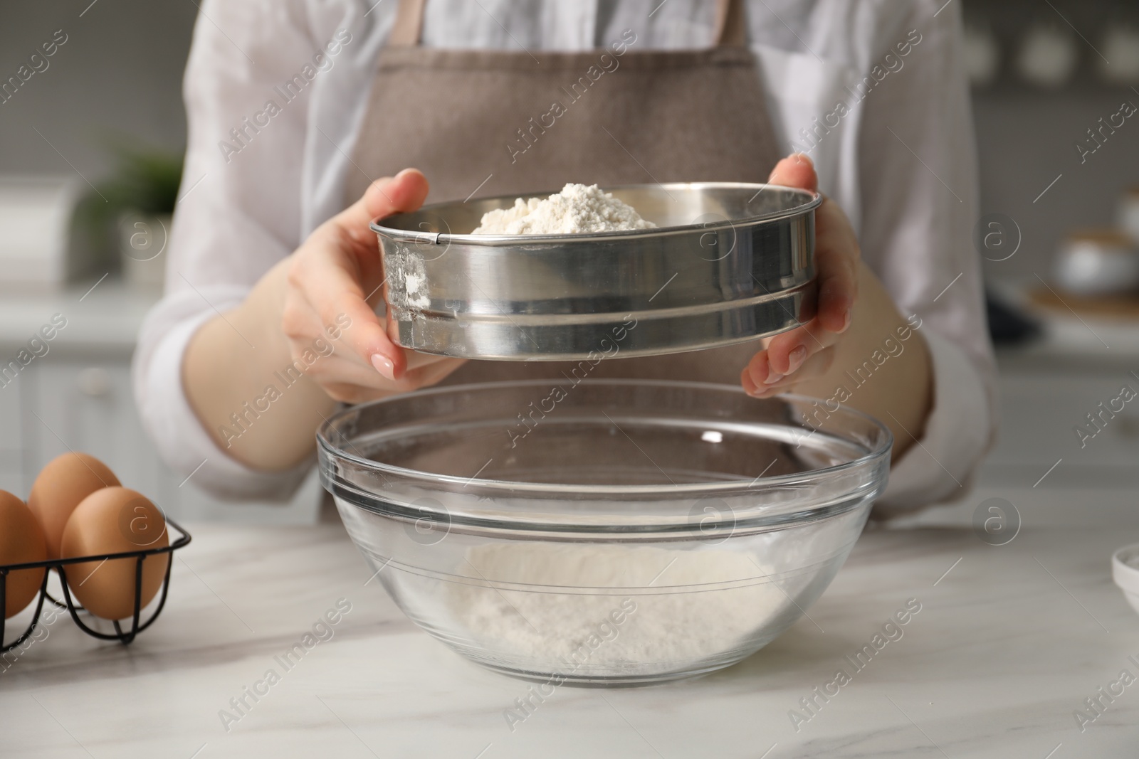 Making pretzels. Woman sieving flour in bowl at table indoors, closeup Photo of Making pretzels. Woman sieving flour in bowl at table indoors, closeup