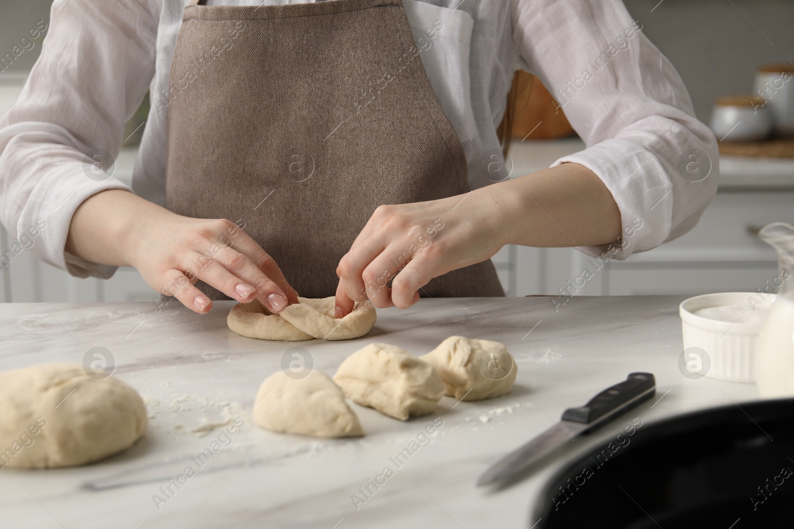 Woman shaping pretzels at table in kitchen, closeup Photo of Woman shaping pretzels at table in kitchen, closeup