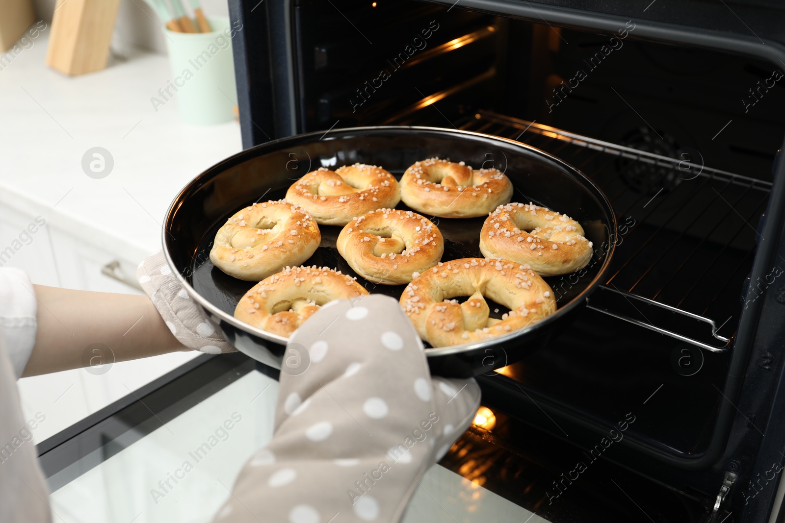 Photo of Woman taking baking dish with fresh pretzels out of oven, closeup