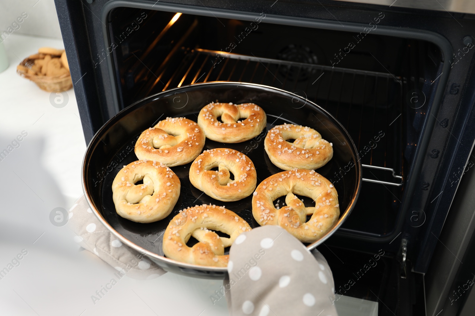 Woman taking baking dish with fresh pretzels out of oven, closeup Photo of Woman taking baking dish with fresh pretzels out of oven, closeup