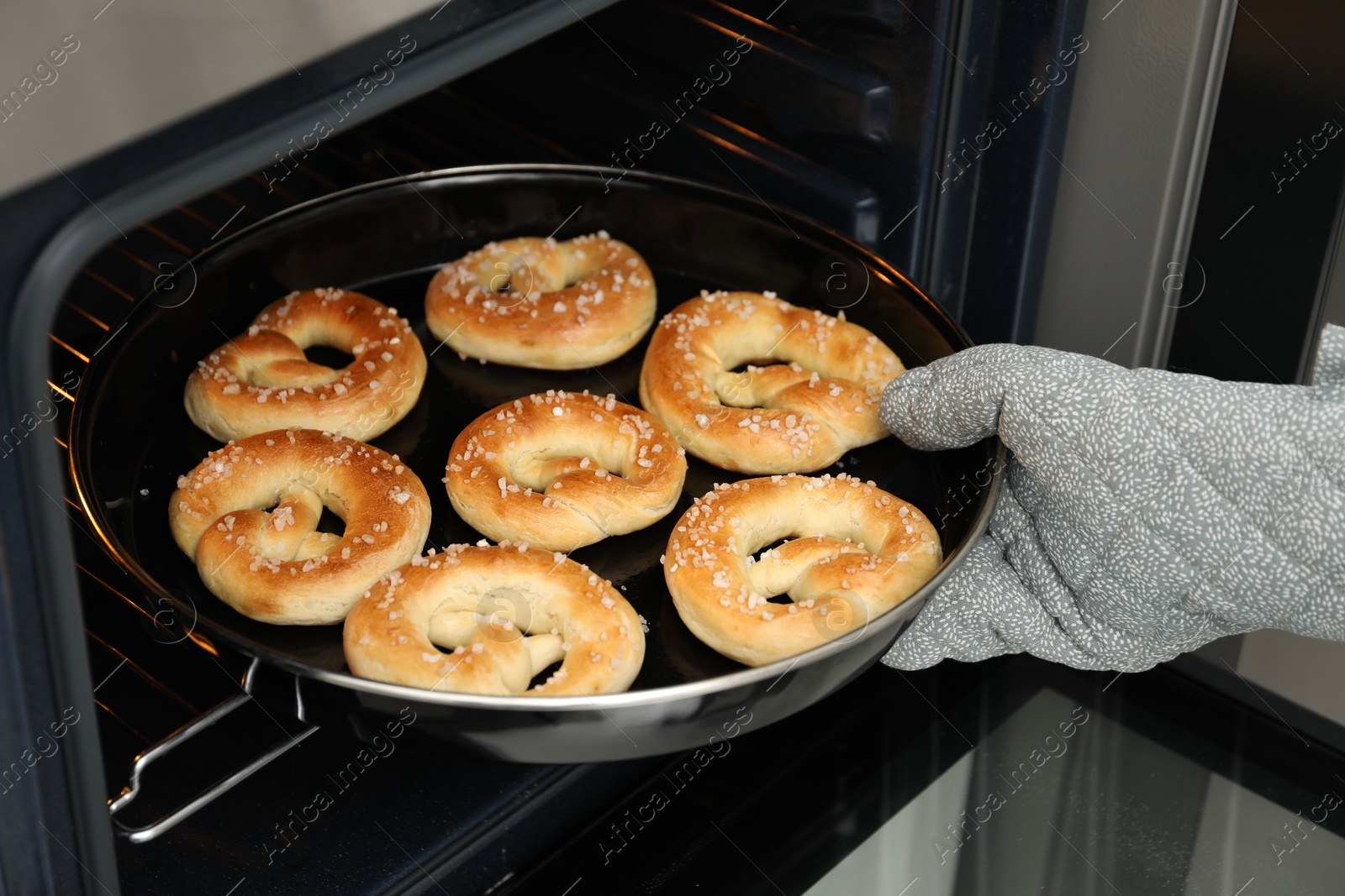 Photo of Woman taking baking dish with fresh pretzels out of oven, closeup