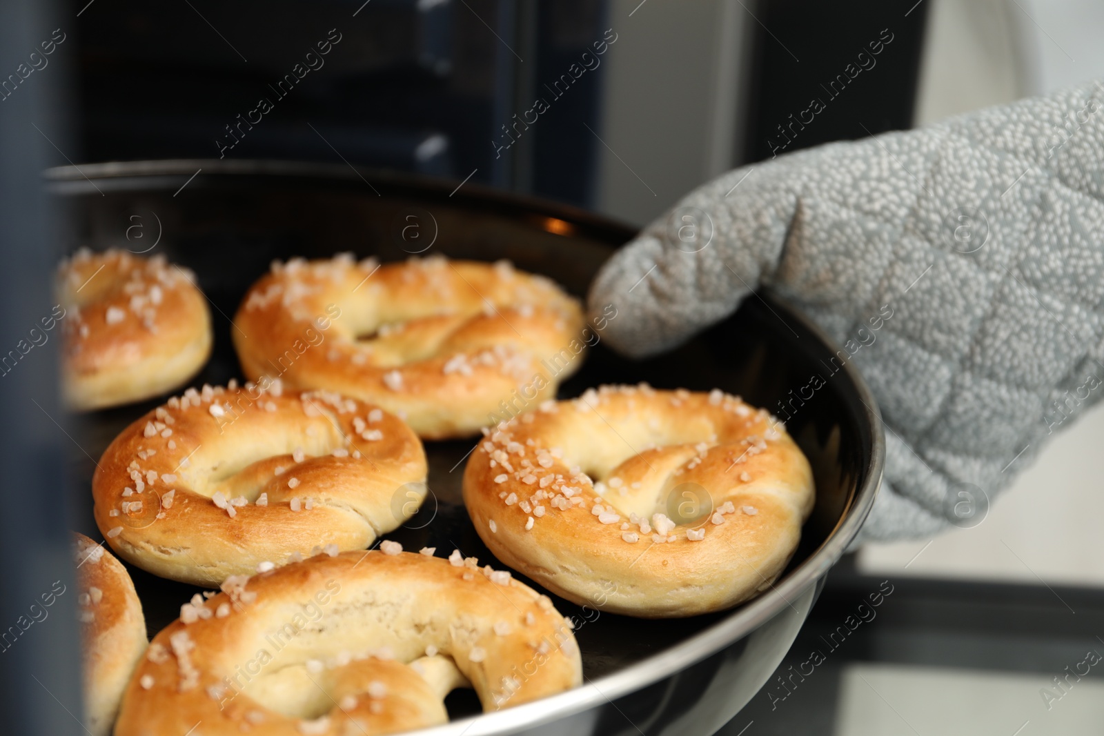 Photo of Woman taking baking dish with fresh pretzels out of oven, closeup