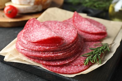 Photo of Slices of tasty smoked sausage and rosemary on black table, closeup