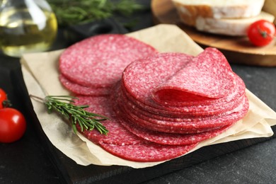Photo of Slices of tasty smoked sausage and rosemary on black table, closeup