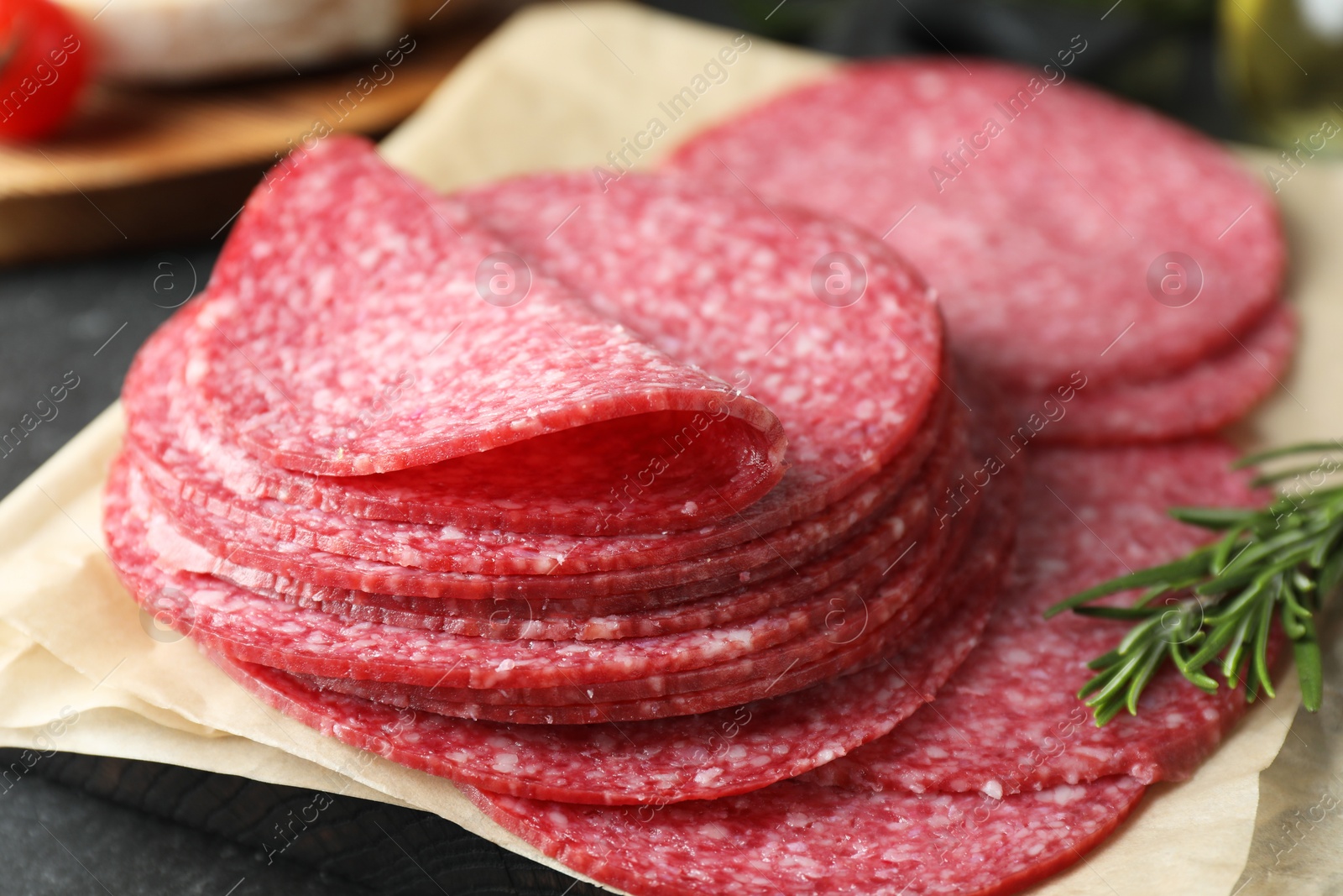 Photo of Slices of tasty smoked sausage and rosemary on table, closeup
