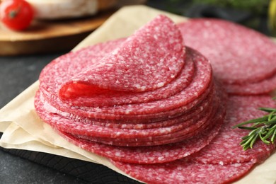 Photo of Slices of tasty smoked sausage and rosemary on black table, closeup