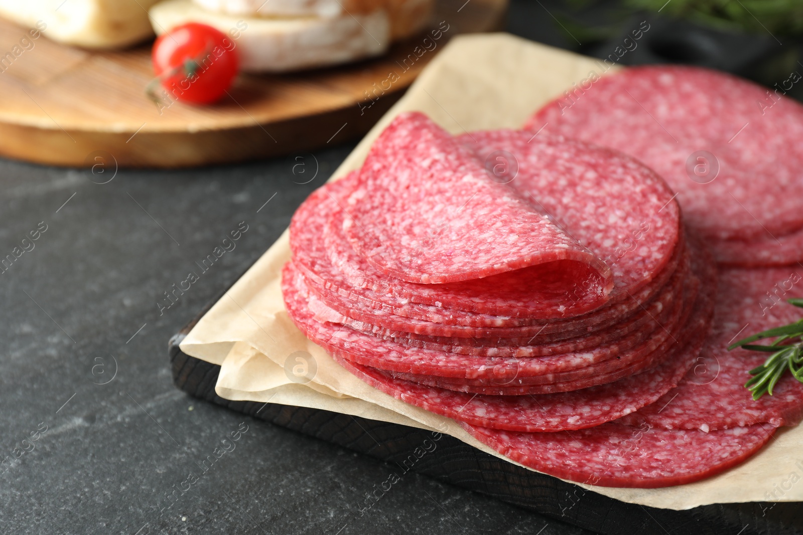 Slices of tasty smoked sausage and rosemary on black table, closeup Photo of Slices of tasty smoked sausage and rosemary on black table, closeup
