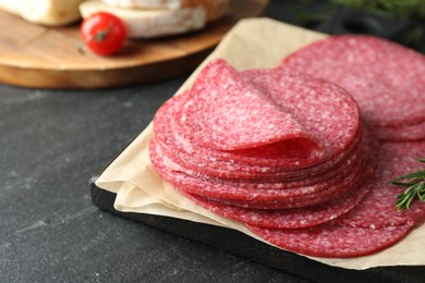 Photo of Slices of tasty smoked sausage and rosemary on black table, closeup