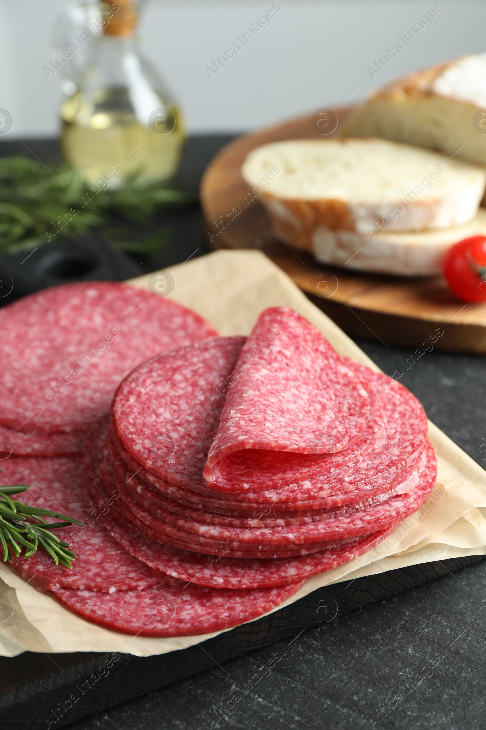 Slices of tasty smoked sausage and rosemary on black table, closeup Photo of Slices of tasty smoked sausage and rosemary on black table, closeup