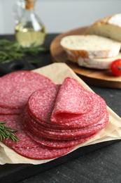 Photo of Slices of tasty smoked sausage and rosemary on black table, closeup