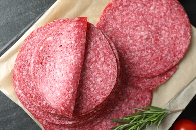 Photo of Slices of tasty smoked sausage and rosemary on black table, top view