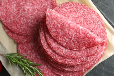 Photo of Slices of tasty smoked sausage and rosemary on black table, top view