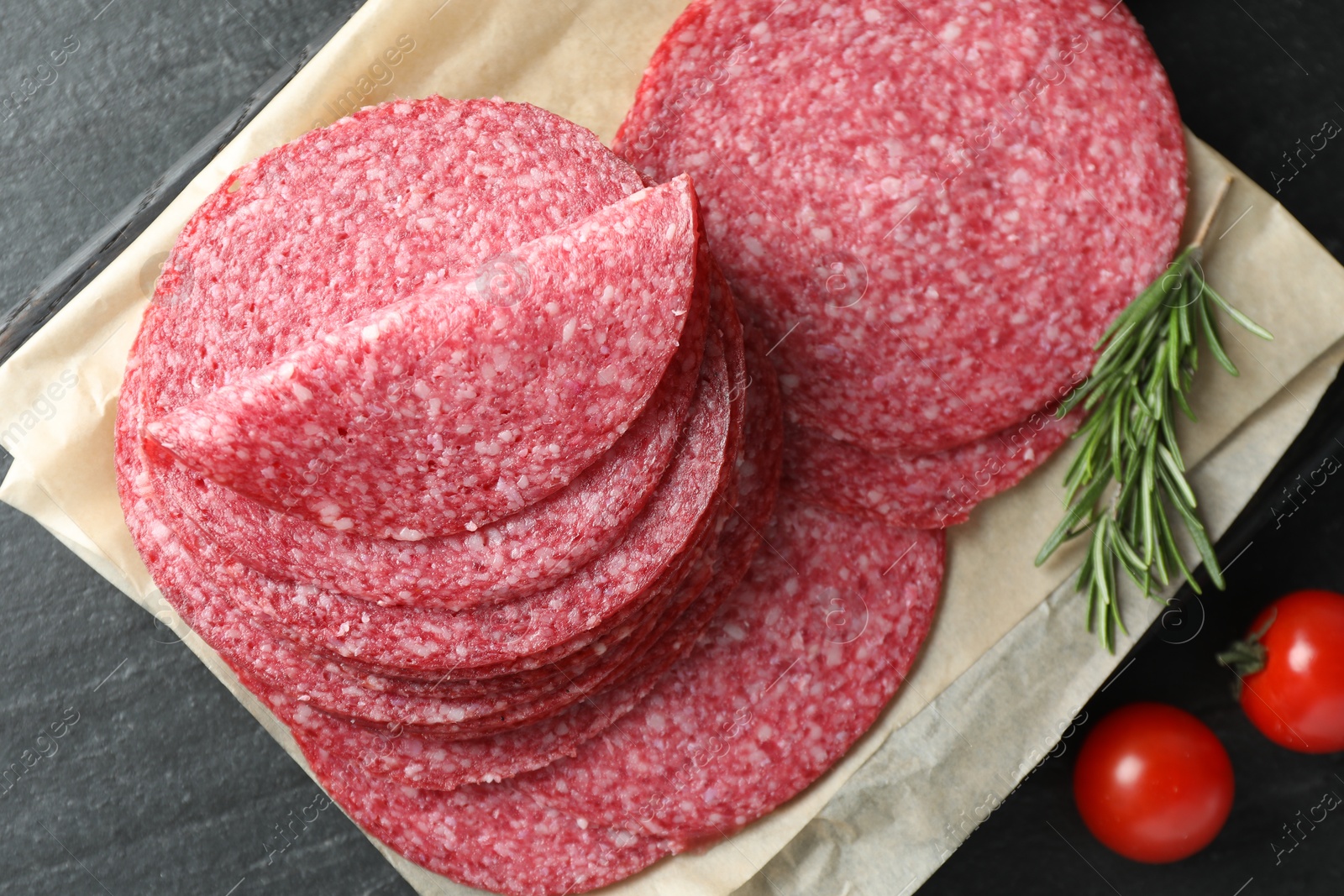 Slices of tasty smoked sausage, rosemary and tomatoes on black table, flat lay Photo of Slices of tasty smoked sausage, rosemary and tomatoes on black table, flat lay