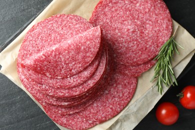 Photo of Slices of tasty smoked sausage, rosemary and tomatoes on black table, flat lay