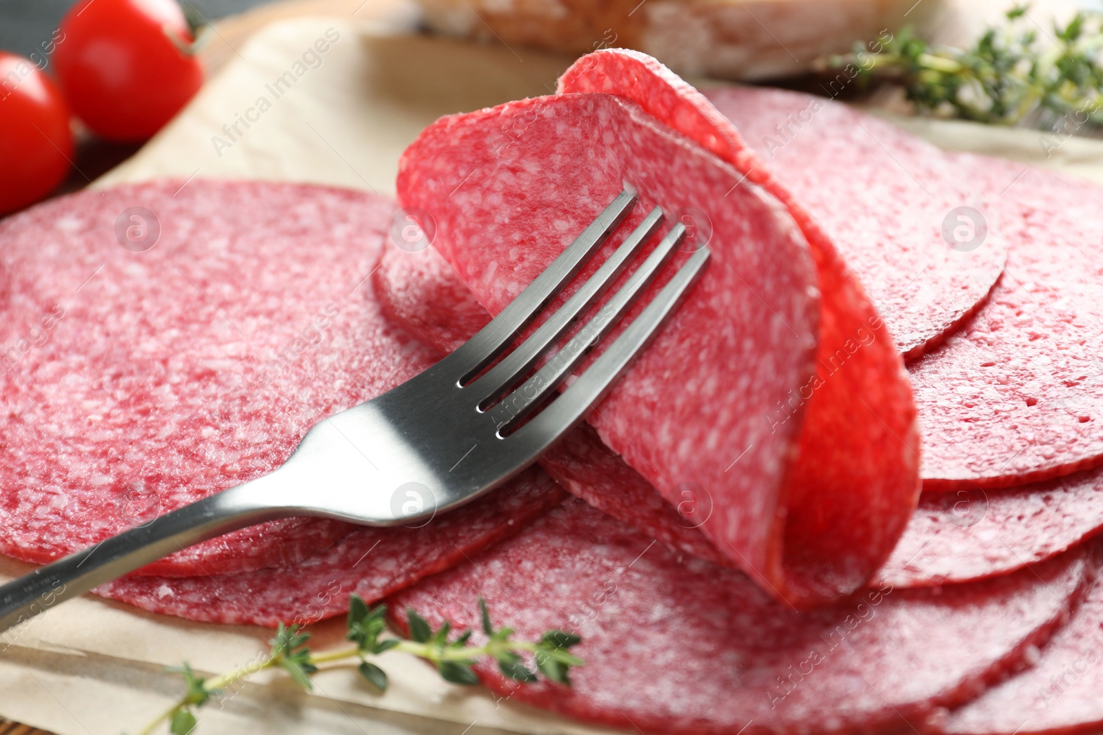 Photo of Slices of tasty smoked sausage, thyme and fork on table, closeup