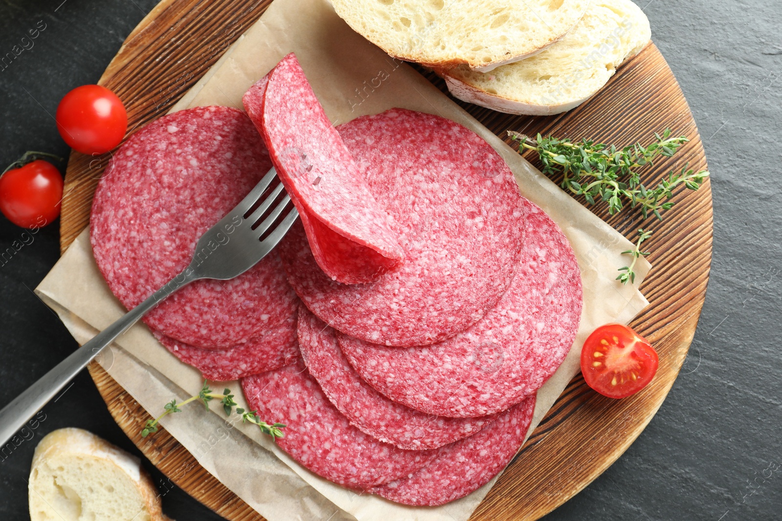 Photo of Slices of tasty smoked sausage, bread, tomatoes and thyme on black table, top view
