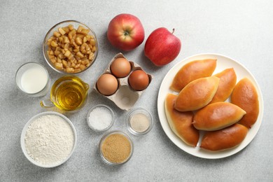 Photo of Tasty baked patties and ingredients on light grey table, flat lay
