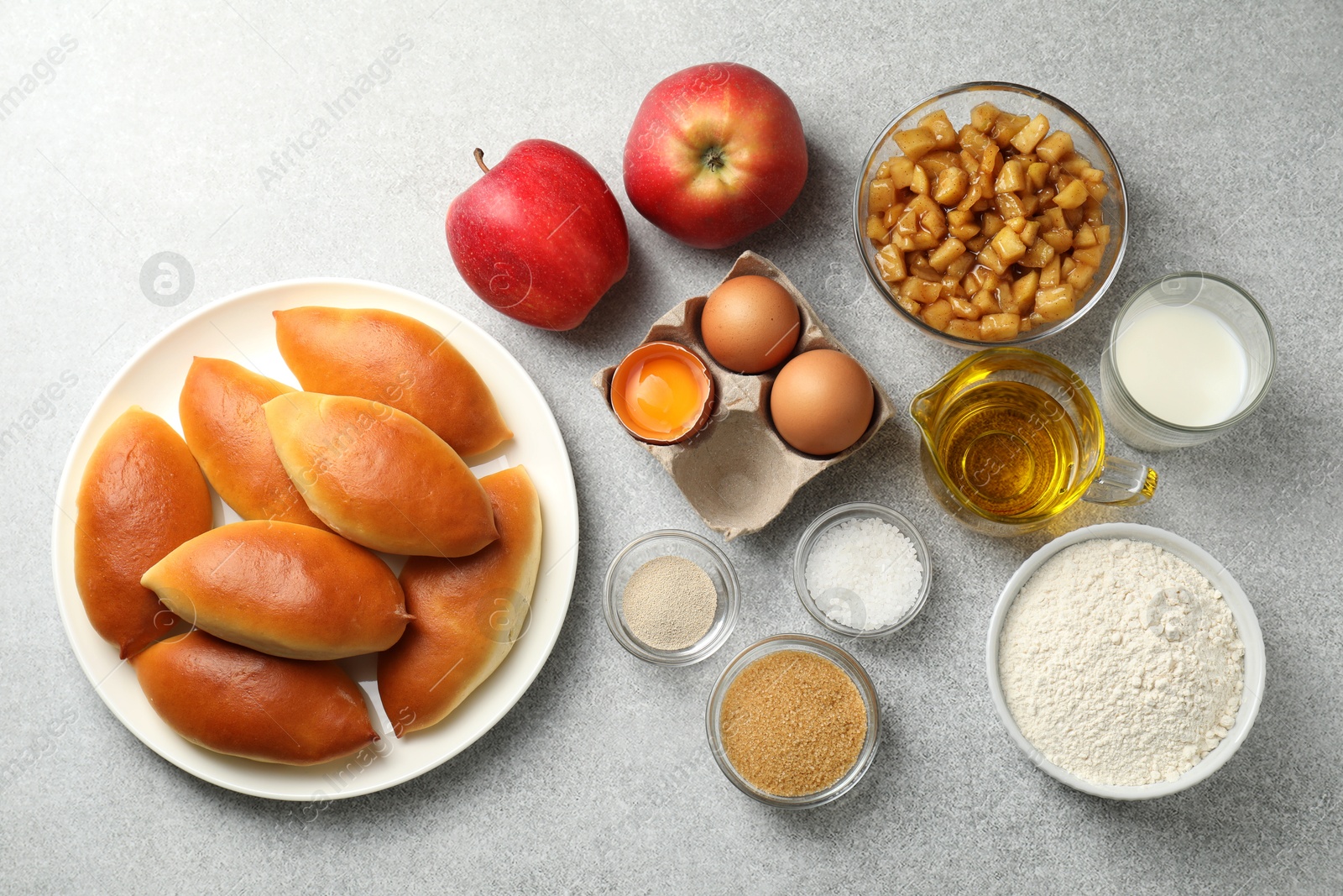 Tasty baked patties and ingredients on light grey table, flat lay Photo of Tasty baked patties and ingredients on light grey table, flat lay