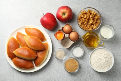 Photo of Tasty baked patties and ingredients on light grey table, flat lay