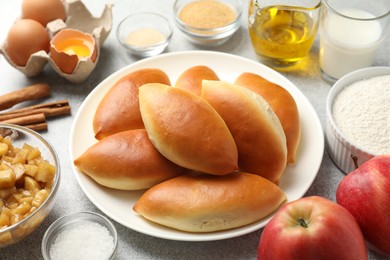 Photo of Tasty baked patties and ingredients on light grey table, closeup