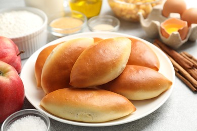 Photo of Tasty baked patties and ingredients on light grey table, closeup