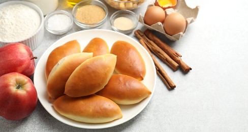 Photo of Tasty baked patties and ingredients on light grey table, closeup. Space for text
