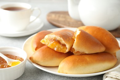 Photo of Tasty baked patties with orange jam on light grey table, closeup