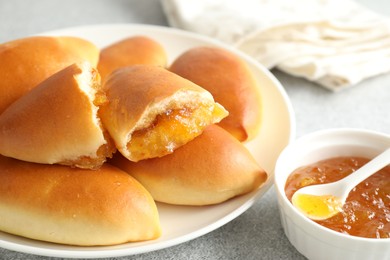 Photo of Tasty baked patties with orange jam on light grey table, closeup