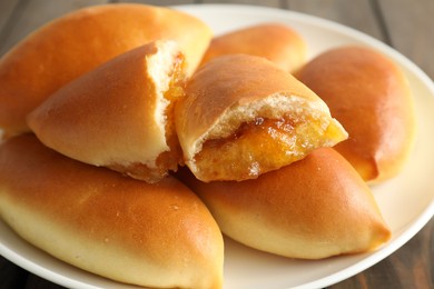 Photo of Tasty baked patties with orange jam on wooden table, closeup