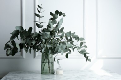 Photo of Green eucalyptus branches in vase on marble table near white wall indoors