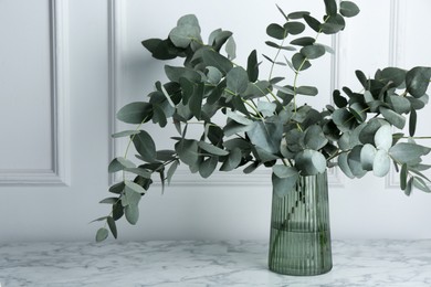 Photo of Green eucalyptus branches in vase on marble table near white wall indoors