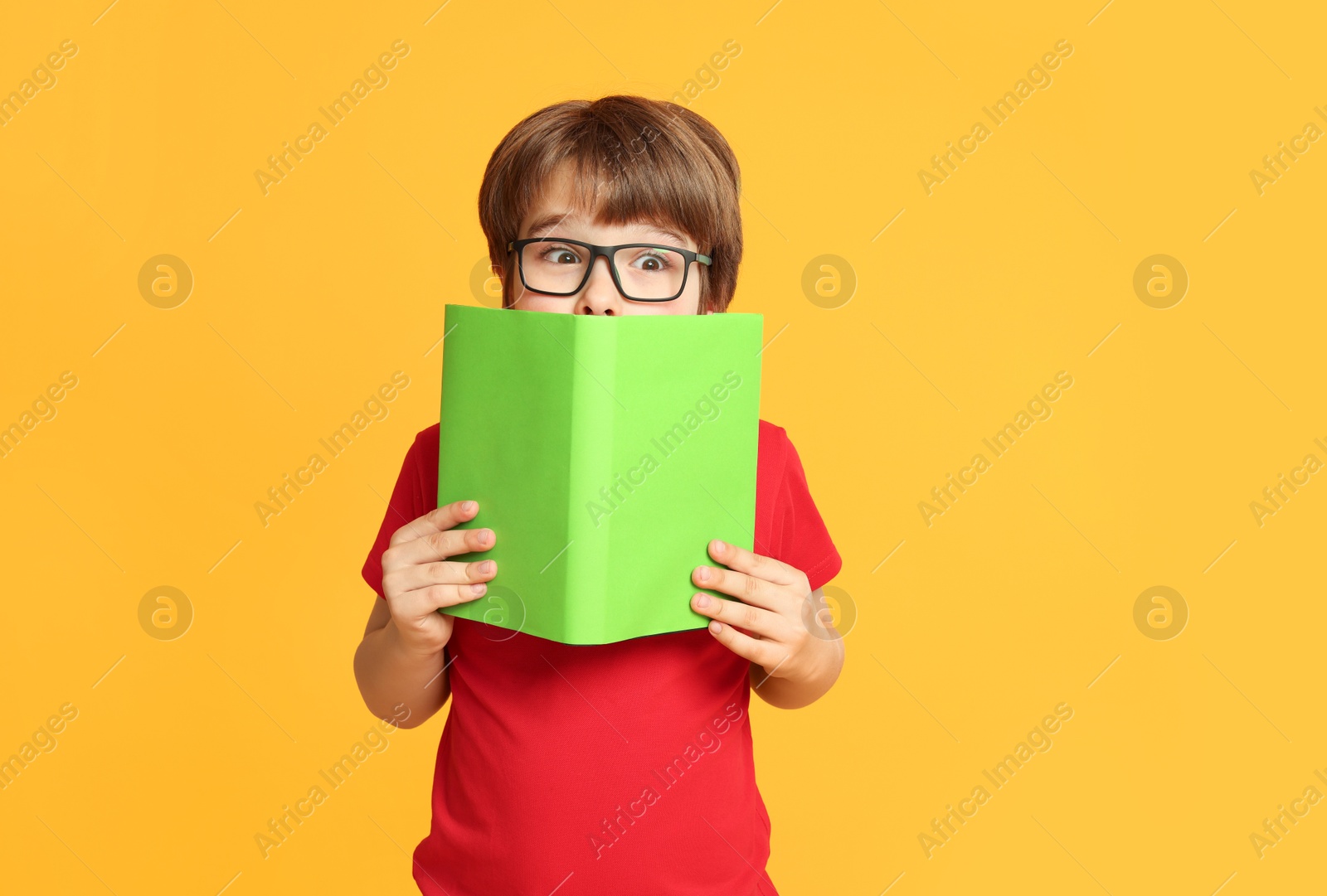 Little boy with book on orange background Photo of Little boy with book on orange background