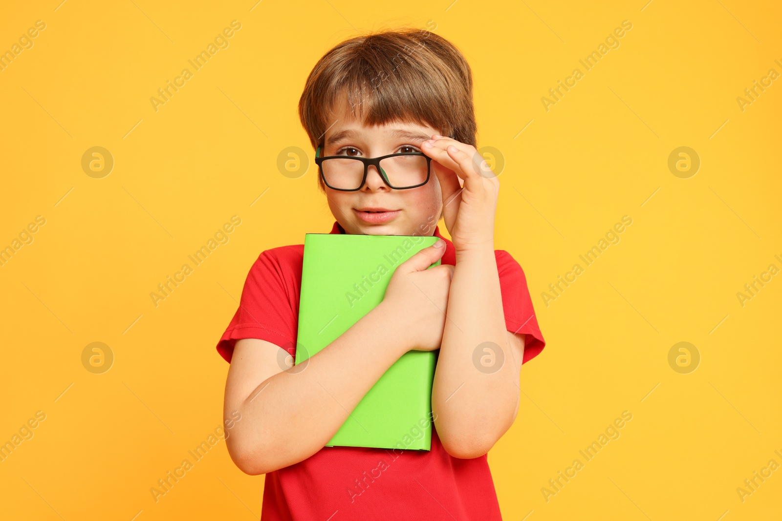 Little boy with book on orange background Photo of Little boy with book on orange background