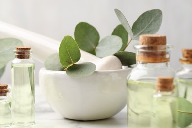 Photo of Bottles of essential oil, eucalyptus leaves, mortar and pestle on table, closeup