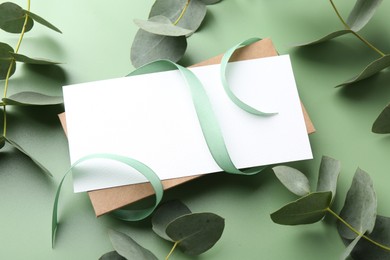 Photo of Blank card, ribbon and eucalyptus branches on light green background, closeup