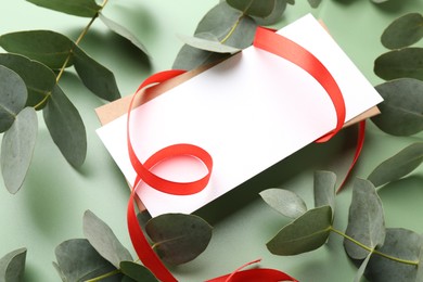 Photo of Blank card, ribbon and eucalyptus branches on light green background, closeup