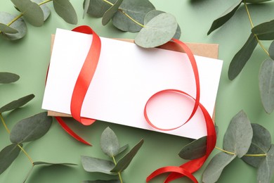 Photo of Blank card, ribbon and eucalyptus branches on light green background, flat lay