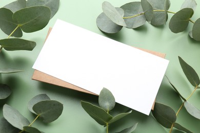 Photo of Blank card and eucalyptus branches on light green background, closeup