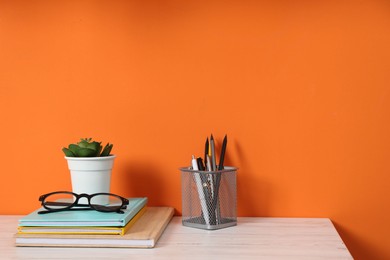 Photo of Stylish workplace with stationery and plant on wooden desk near orange wall. Space for text