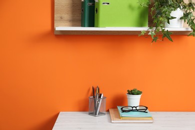 Photo of Stylish workplace with stationery and plant on wooden desk near orange wall. Space for text