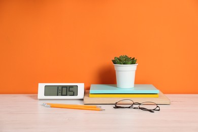 Photo of Stylish workplace with stationery and plant on wooden desk near orange wall. Space for text
