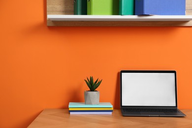 Photo of Stylish workplace with modern laptop on wooden desk near orange wall. Space for text