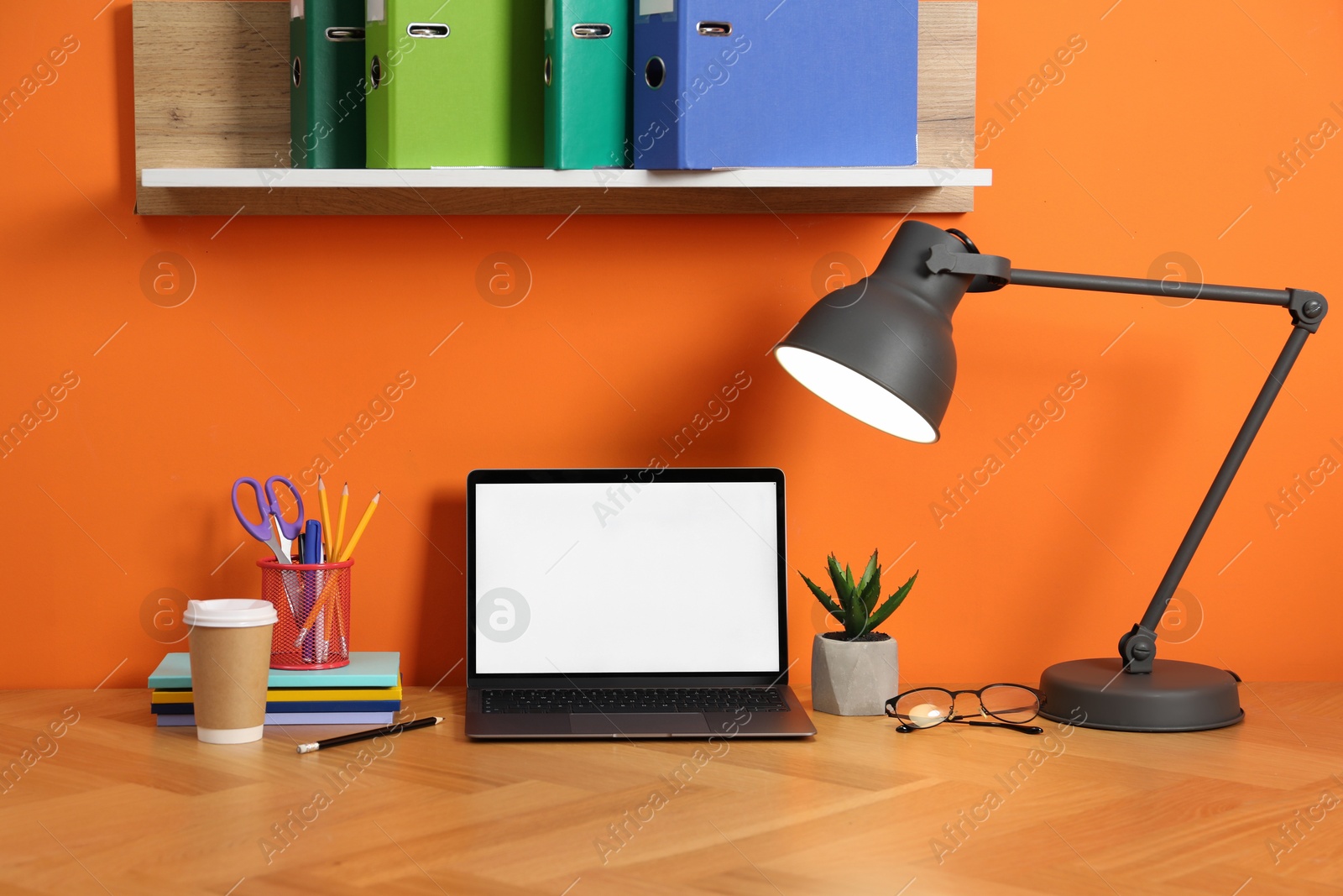 Stylish workplace with modern laptop on wooden desk near orange wall Photo of Stylish workplace with modern laptop on wooden desk near orange wall