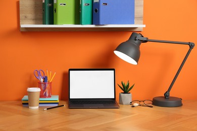 Photo of Stylish workplace with modern laptop on wooden desk near orange wall