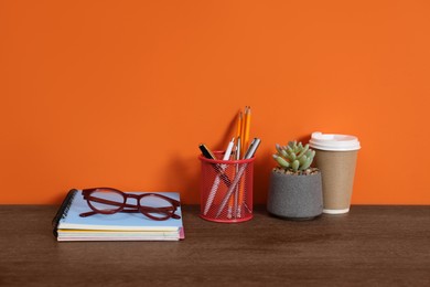 Photo of Stylish workplace with stationery, coffee and plant on wooden desk near orange wall. Space for text