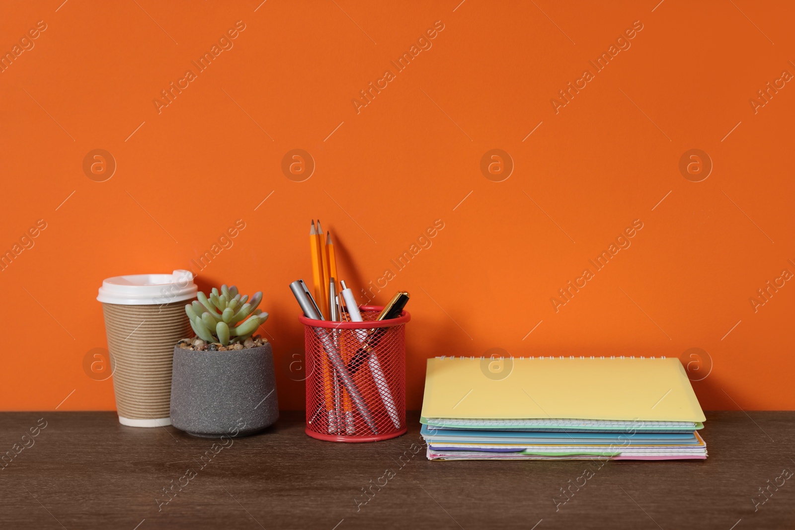 Stylish workplace with stationery, coffee and plant on wooden desk near orange wall. Space for text Photo of Stylish workplace with stationery, coffee and plant on wooden desk near orange wall. Space for text