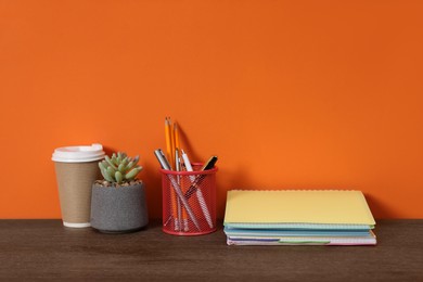 Photo of Stylish workplace with stationery, coffee and plant on wooden desk near orange wall. Space for text