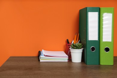 Photo of Stylish workplace with stationery and plant on wooden desk near orange wall. Space for text