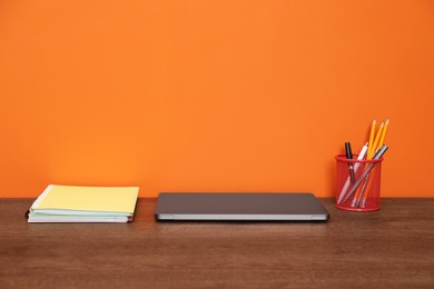 Photo of Stylish workplace with modern laptop on wooden desk near orange wall. Space for text