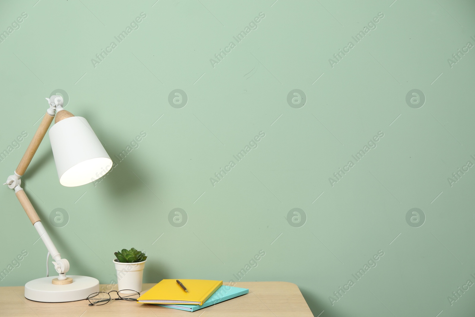 Stylish workplace with lamp, stationery and plant on wooden desk near light green wall. Space for text Photo of Stylish workplace with lamp, stationery and plant on wooden desk near light green wall. Space for text